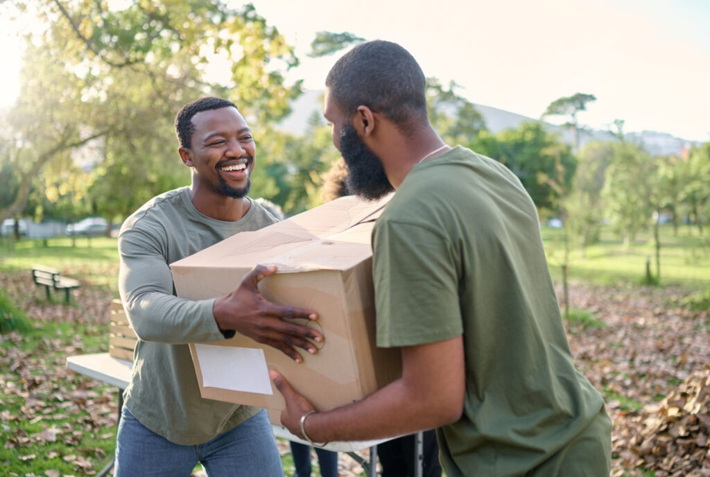 Black man, charity and holding box in park of donation, community service or social responsibility. Happy guy, NGO workers and team helping with package for volunteering, support and society outreach.